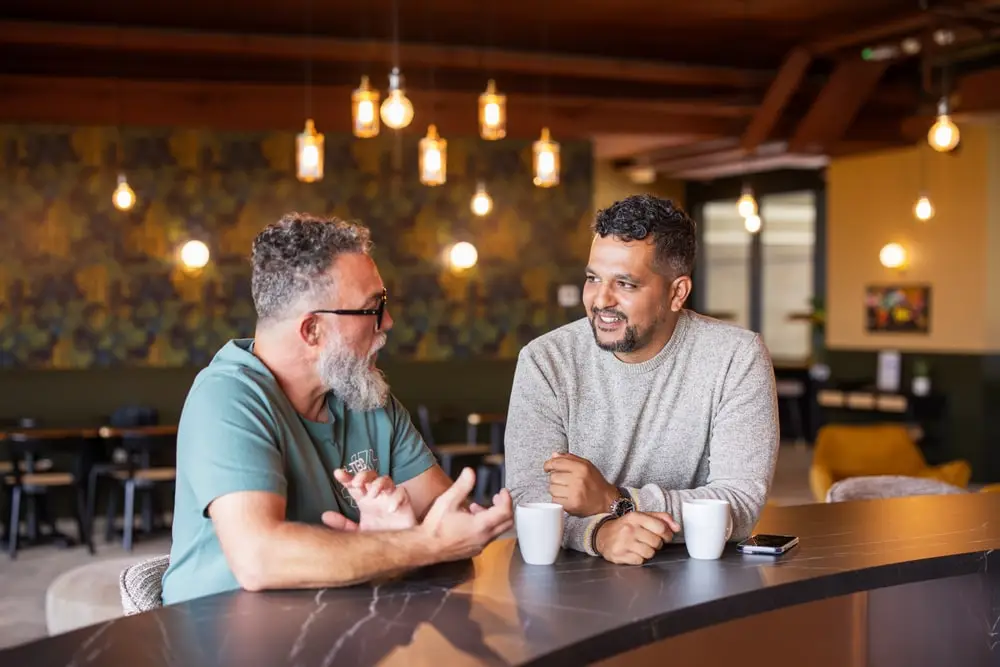 Sofiane Hamiti en discussion avec un client autour d'un café, dans un espace de travail partagé.
